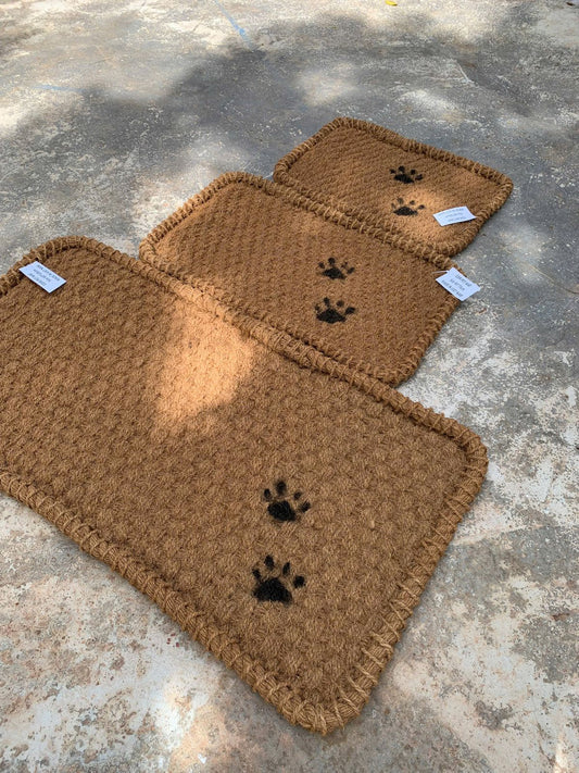 Three brown dog mats with black paw prints on a concrete surface